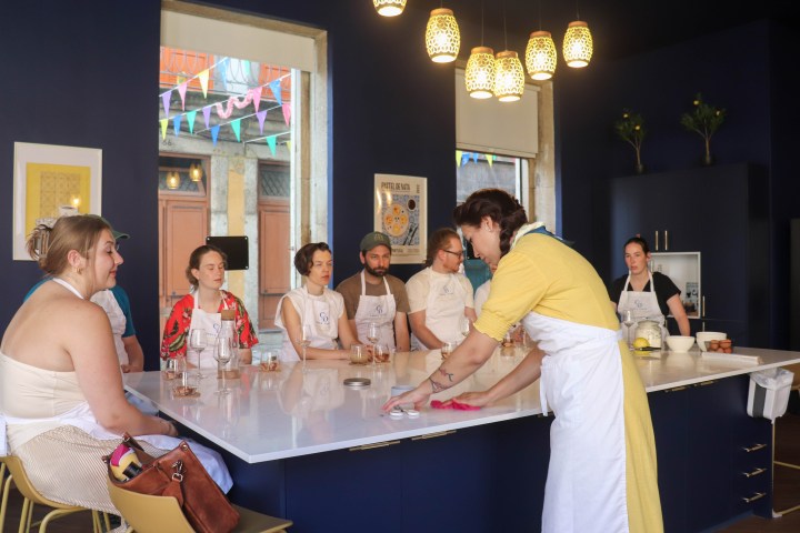 Class in a kitchen with a teacher wiping a counter as students watch attentively.