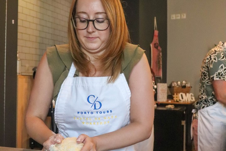 Woman kneading dough at a workshop, wearing glasses and an apron.