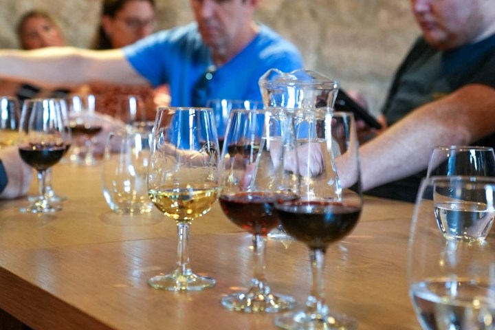 People at a table with assorted wine glasses and a water jug in a rustic setting.