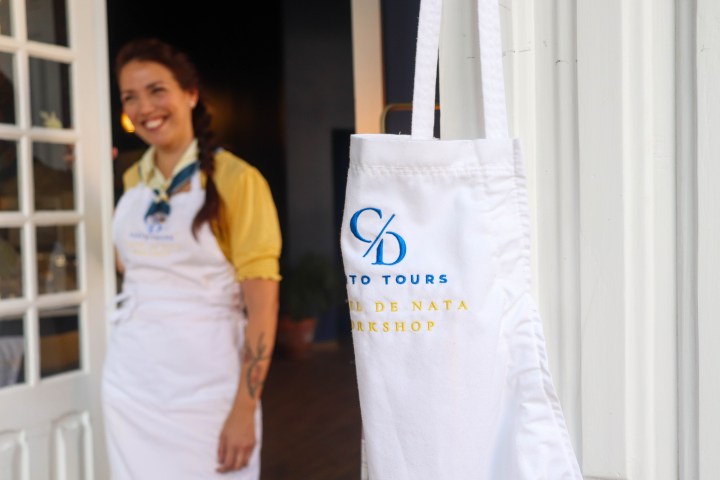 Smiling person in apron near door, close-up of apron text: 'CD Tours, Pastel de Nata Workshop'.