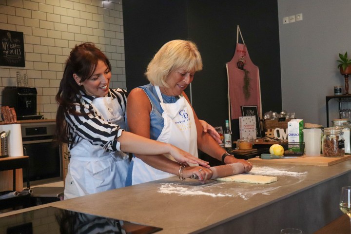 Two women smiling while rolling dough together in a kitchen.