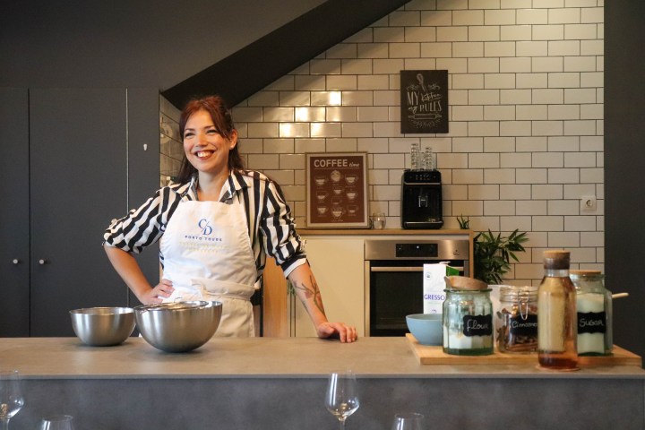 Smiling woman in apron stands in modern kitchen with baking supplies on counter.