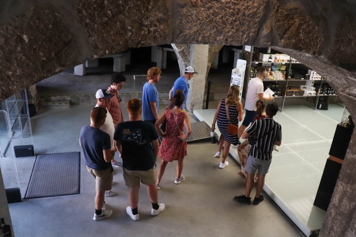 People gather under an arch, near a store with shelves, wearing casual summer clothes.