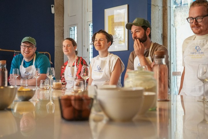 Five people wearing aprons seated around a table with drinks, in a room with blue walls.