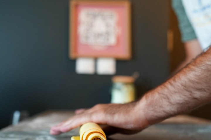 Person rolling yellow dough on a floured countertop, focus on hands and dough.