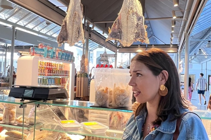 Woman in denim jacket at fish market with dried fish hanging and a display case.