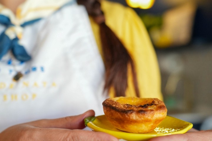 Person holding a yellow plate with a pastry tart, wearing a white apron with braided hair.
