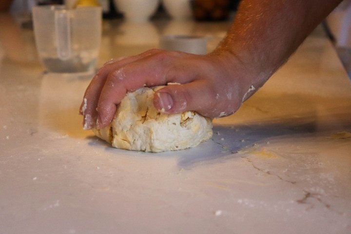 Hand kneading dough on a floured surface with kitchen items in background.