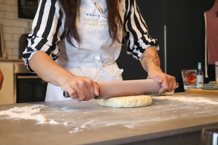 Person rolling dough on a floured surface with a rolling pin in a kitchen.