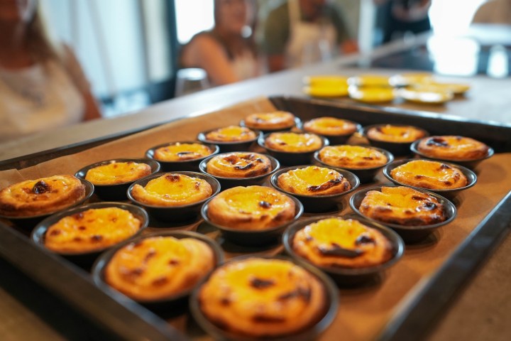 Tray of freshly baked custard tarts with people blurry in the background.