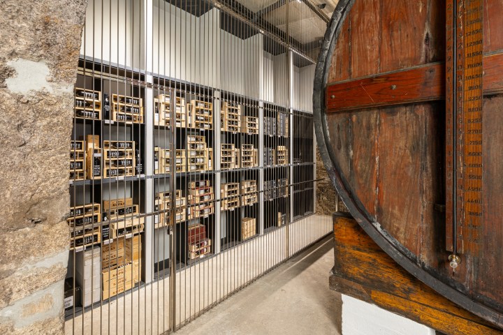 Industrial storage room with shelves of wooden crates behind bars and a large wooden barrel.