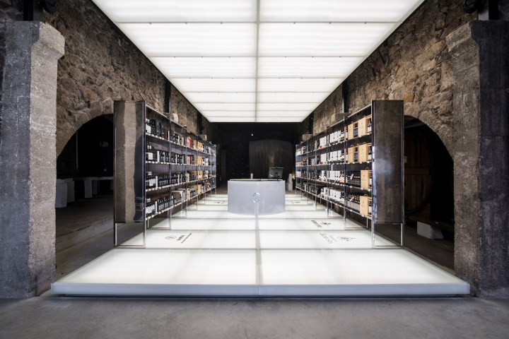 Modern wine cellar with glass floor and stone walls, featuring shelves of wine bottles.