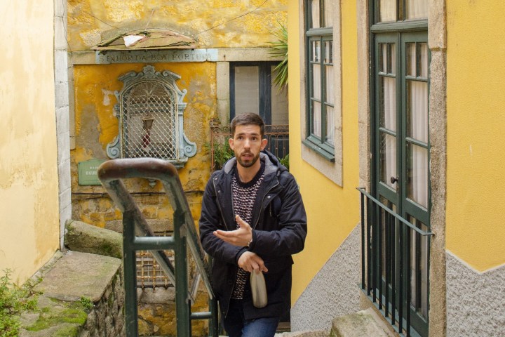 Man in black jacket on stone steps between yellow buildings.