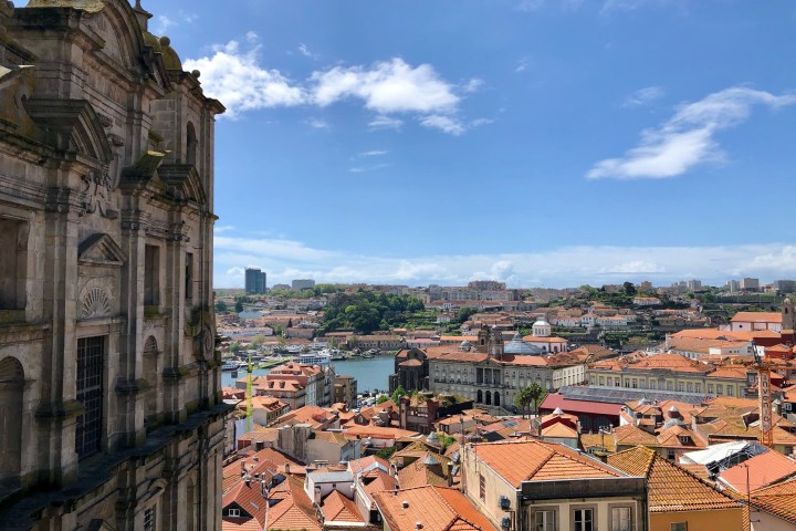Cityscape with historic building, red rooftops, river, and clear blue sky.