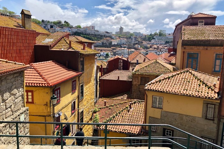 View of colorful buildings with red-tiled roofs on a hillside under a cloudy sky.