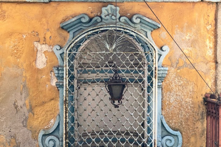 Rustic window with sign 'Senhor da Boa Fortuna' on yellow wall, iron grill, and green street sign.
